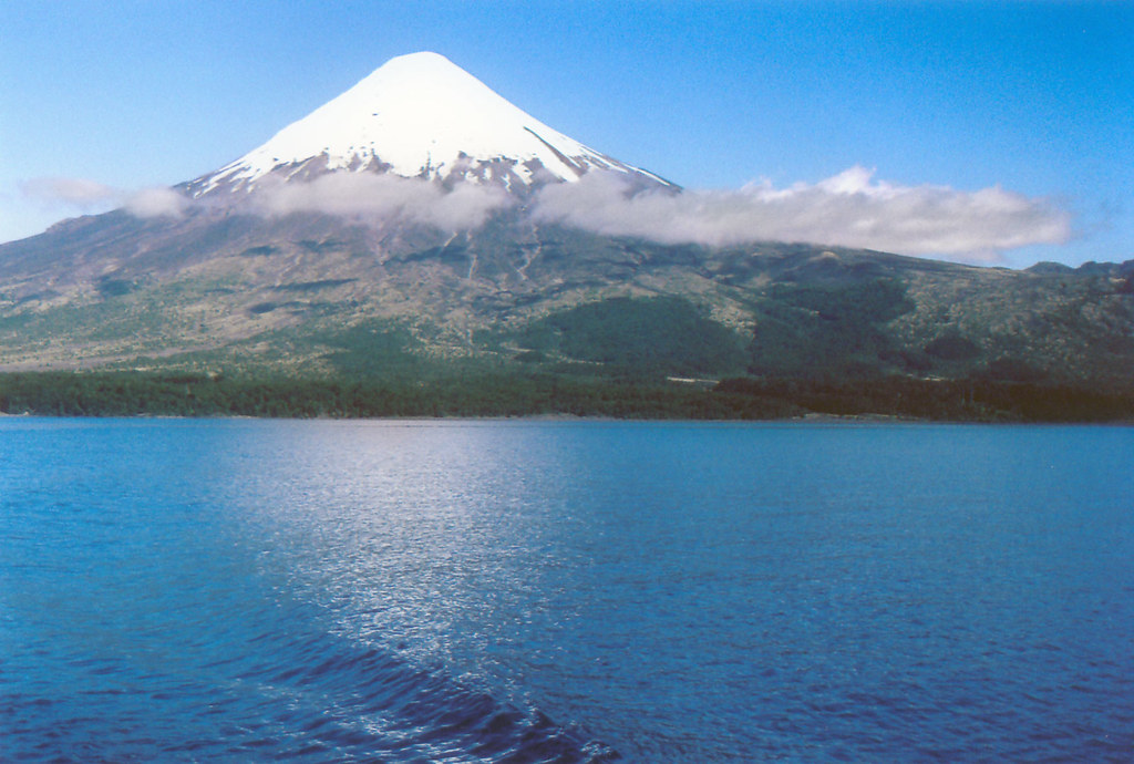 Snow-capped volcano rising above a deep blue lake in Chile’s Lake District
