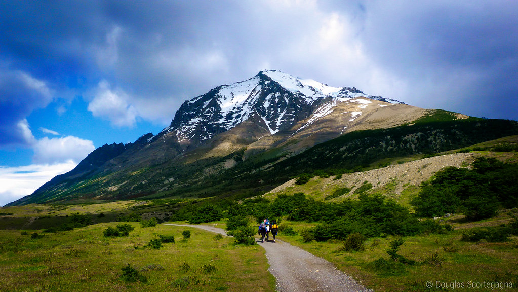 Two hikers walking a gravel trail toward a snow-covered mountain in Torres del Paine